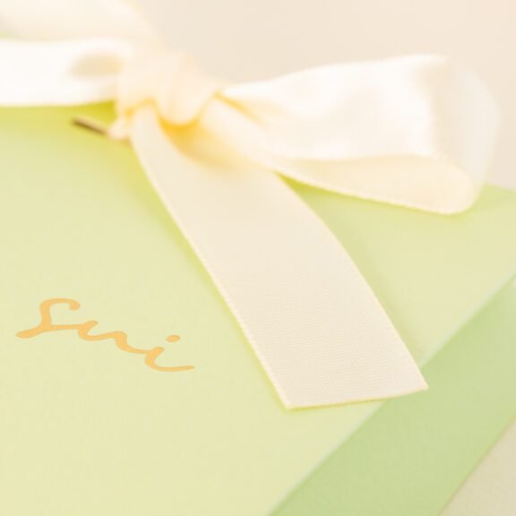 Green gift box with "Amor Sui" written in elegant gold script and adorned with a white satin ribbon bow.